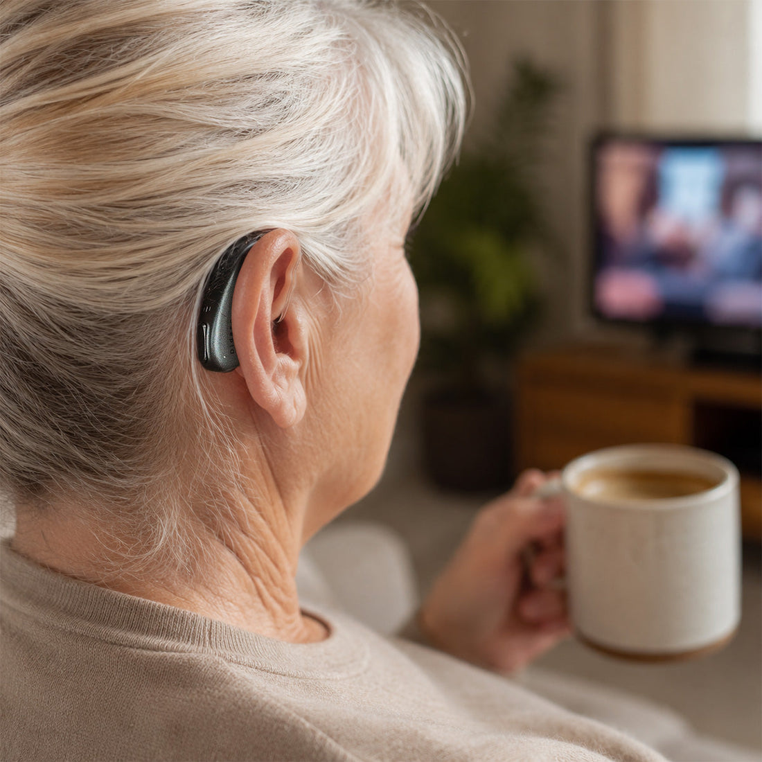 Older woman wearing a RIC hearing aid while watching TV and holding a cup at home.